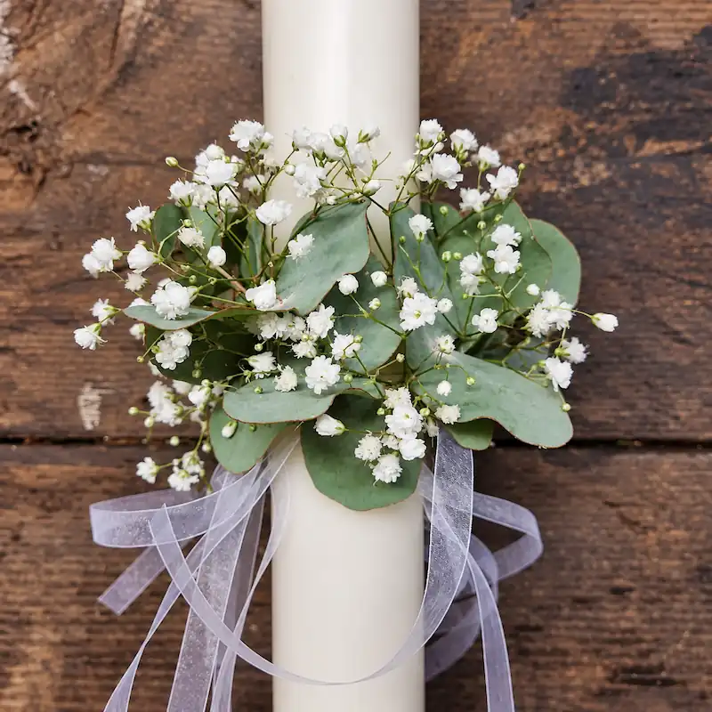 Décoration florale de baptême avec gypsophile blanc et eucalyptus autour d’un cierge